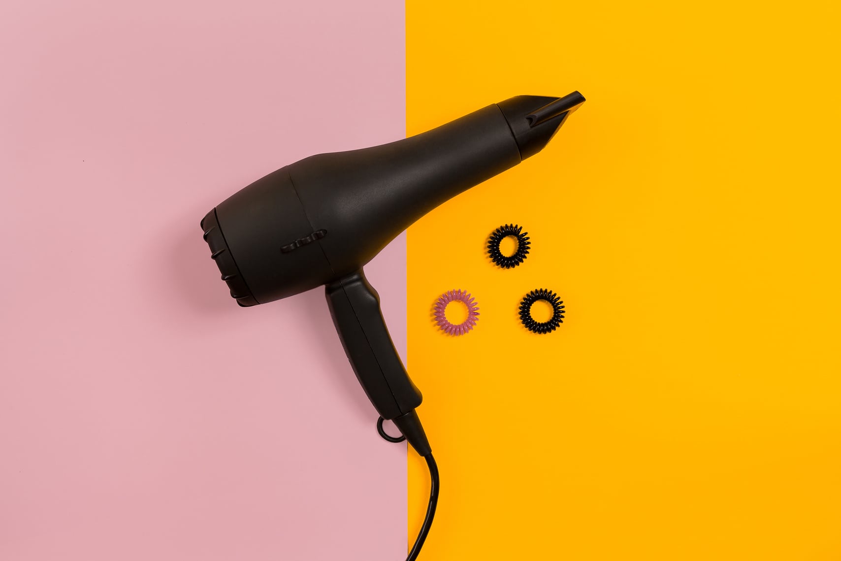 Black Hair Dryer on Pink and Yellow Paper Background. Top View